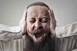 close up photo of screaming man with a full beard covering his ears and closing his eyes